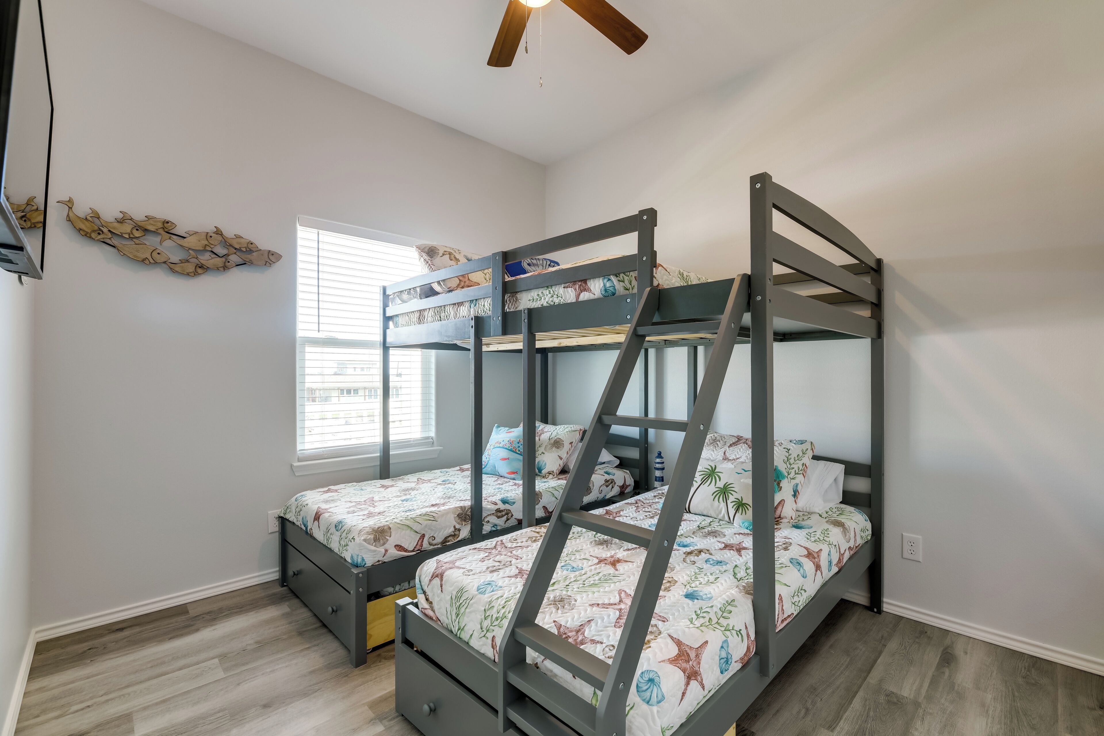 Un dormitorio con literas, ventilador de techo, ventana con persianas y un adorno de pared.
