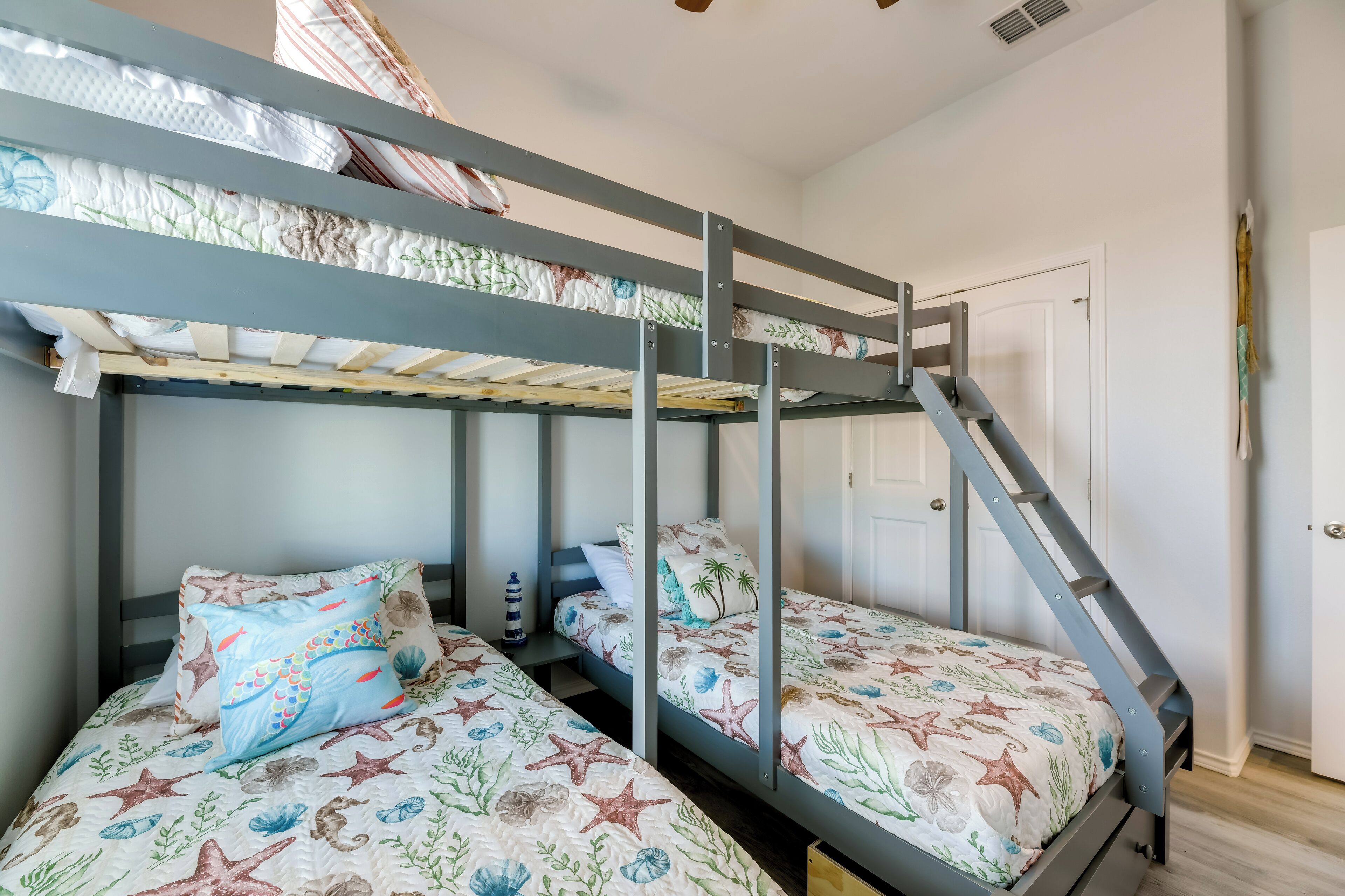 Ein Mehrbettzimmer mit zwei Betten, jedes mit einer Bettdecke im Stil eines Seesterns. Eine Treppe führt zum oberen Bett.