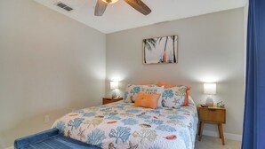 A bedroom with a bed, nightstands, a ceiling fan, a wall-mounted lamp, and a beach-themed painting. - Near Beach! Modern Ground-floor Condo in St Pete (St. Pete Beach)