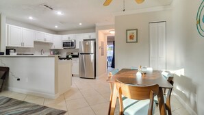 A modern kitchen with white cabinets, stainless steel appliances, and a dining area with a wooden table and chairs. - Near Beach! Modern Ground-floor Condo in St Pete (St. Pete Beach)