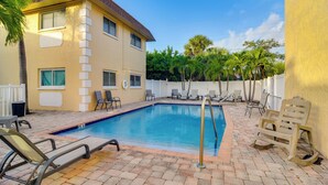 A swimming pool with lounge chairs, a building with a tiled roof, and palm trees. - Near Beach! Modern Ground-floor Condo in St Pete (St. Pete Beach)