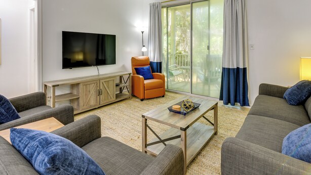 A modern living room with a flat-screen TV, two sofas, a coffee table, a wooden cabinet, and a chair with a cushion. - Prime Miramar Beach Getaway w/ Pool Access! (Miramar Beach)