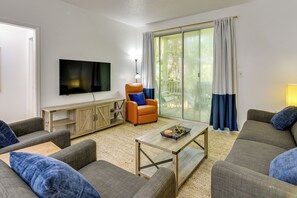 A modern living room with a flat-screen TV, two sofas, a coffee table, a wooden cabinet, and a chair with a cushion. - Prime Miramar Beach Getaway w/ Pool Access! (Miramar Beach)