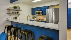 A modern kitchen with blue cabinets, stainless steel appliances, and a bar area with stools. - Prime Miramar Beach Getaway w/ Pool Access! (Miramar Beach)