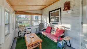 A covered porch with a wooden table, two chairs, a bench with red cushions, and a window with blinds. - Cozy Pennsylvania Home w/ Fire Pit & Dock Access! (Carbondale)