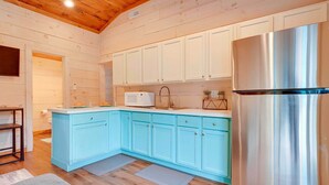 A modern kitchen with light blue cabinets, a stainless steel refrigerator, and wooden flooring. - Lovely Au Gres Cottage w/ Hot Tub: Walk to Beach! (Au Gres)