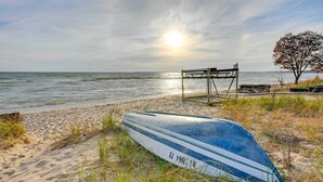 A beach with a boat, a bench, and a tree. - Lovely Au Gres Cottage w/ Hot Tub: Walk to Beach! (Au Gres)