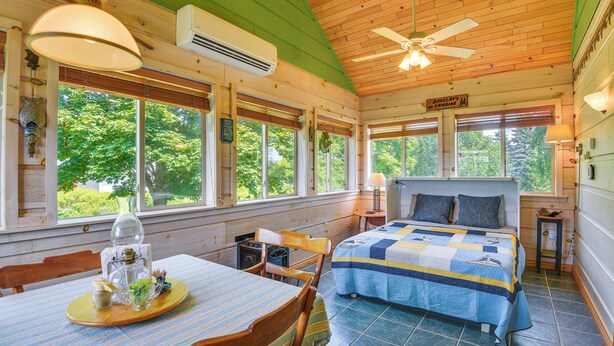 Ein gemütliches Blockhauskabinen-Interieur mit Bett, Esstisch und großen Fenstern mit Blick ins Freie.