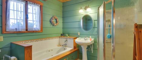 Ein Badezimmer mit einer Holzbadewanne, einem Standwaschbecken, einer Duschkabine aus Glas und einem Fenster mit Vorhängen.