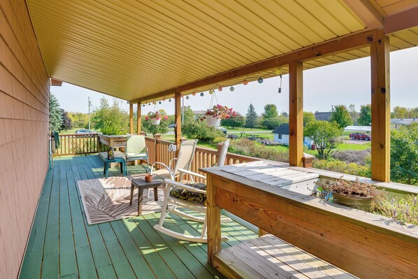 A covered deck with a wooden table, chairs, and hanging flower pots. - Warm & Cozy Clayton Cabin Near St Lawrence River! (Clayton)