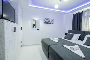 A modern hotel room with a large bed, a flat-screen TV mounted on a marble wall, a bedside table, and a ceiling light. - Jensila Suite (Zakynthos)