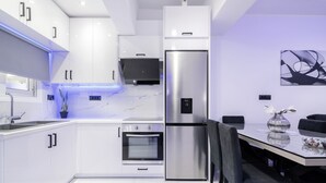 A modern kitchen with white cabinetry, stainless steel appliances, and a dining area with a marble countertop and black chairs. - Jensila Suite (Zakynthos)