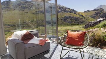 A modern room with a glass wall offering a mountain view, a grey sofa, and a wicker chair.