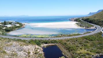 Vista aérea de uma área costeira com uma estrada sinuosa, uma praia e uma pequena massa de água.