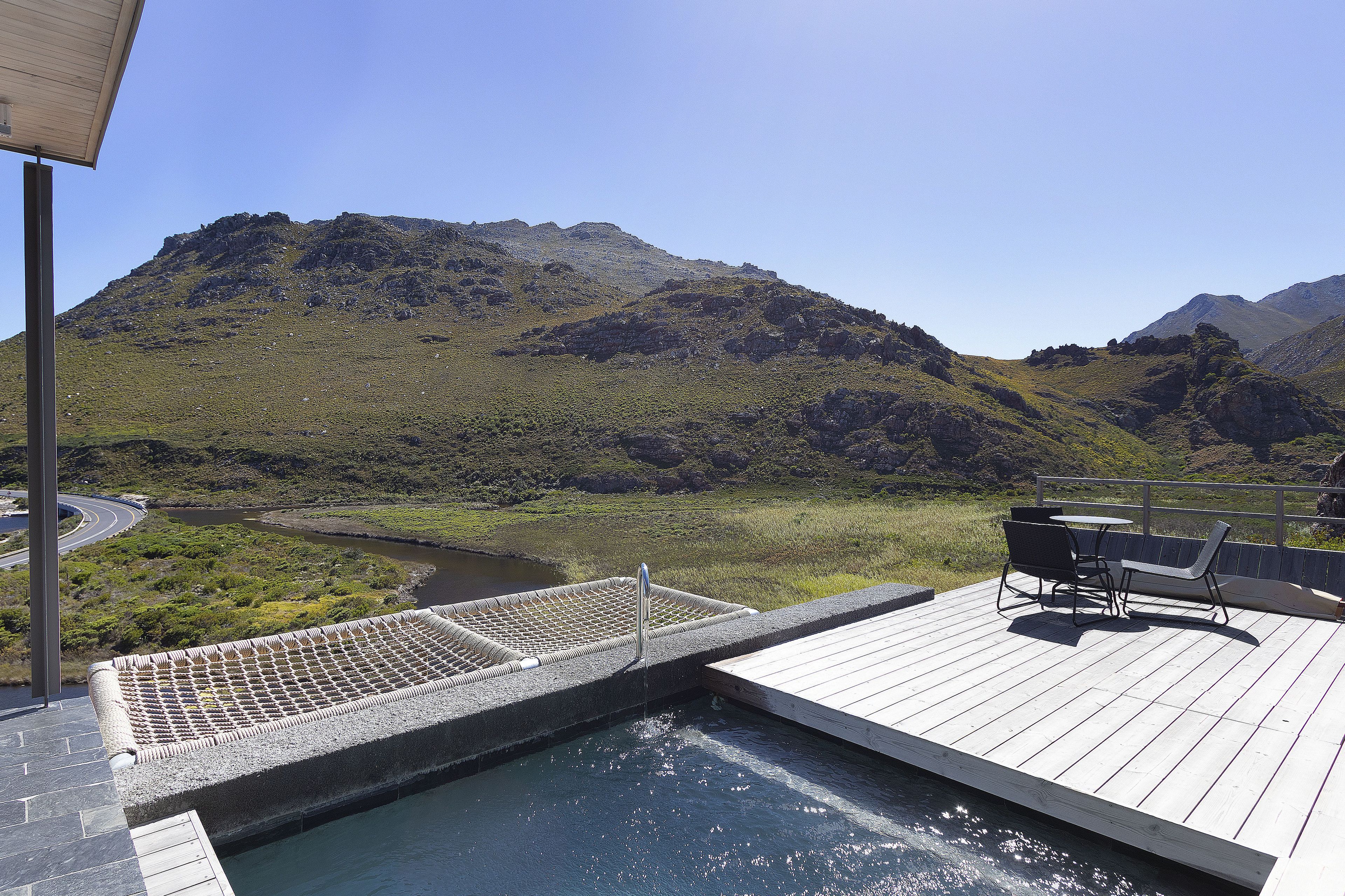 Zona de piscina con vistas a montañas, una terraza con mobiliario exterior y una fuente de agua.