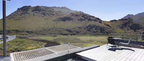 A pool area with a view of mountains, a deck with outdoor furniture, and a water feature.