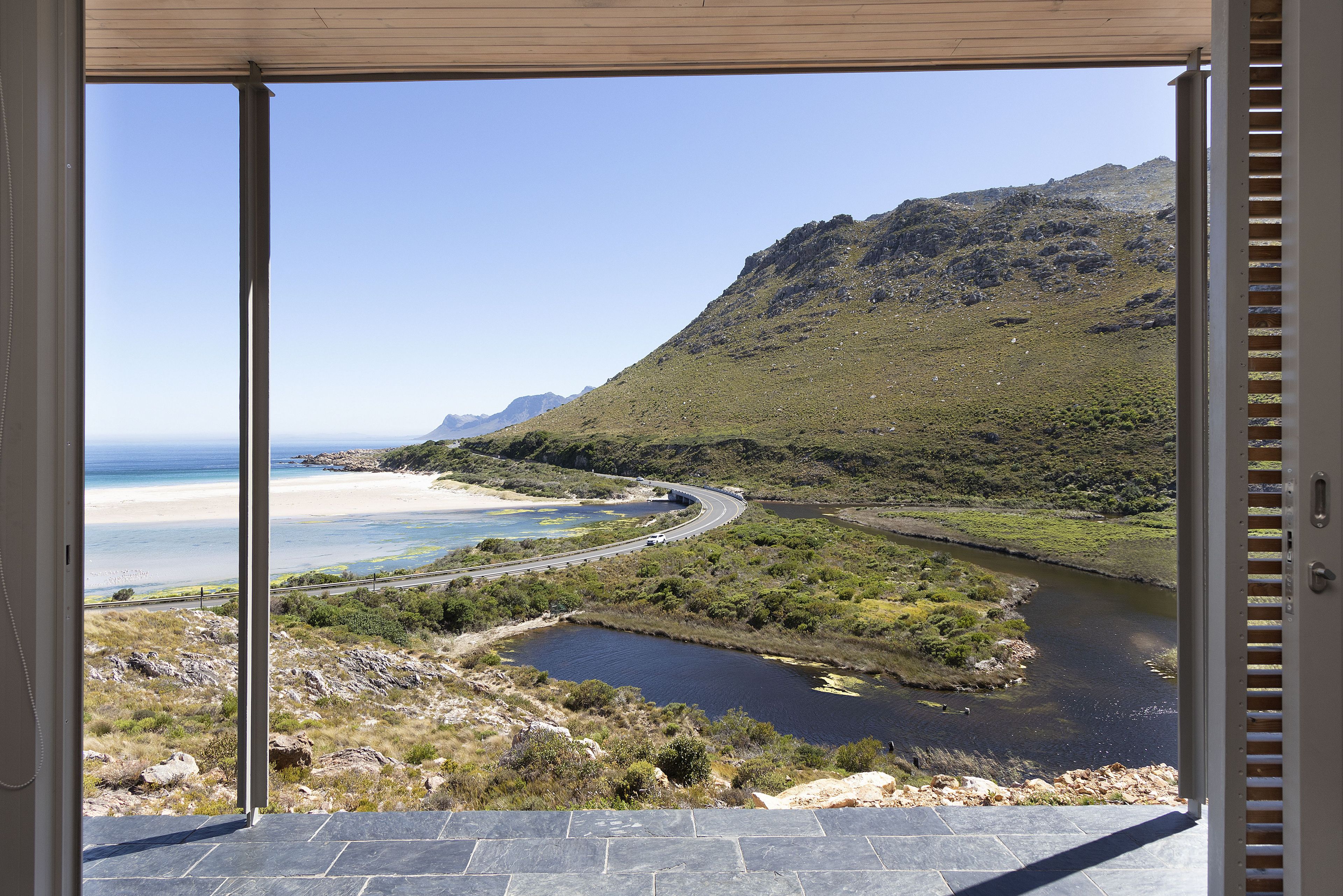 A view from a balcony overlooking a coastal landscape with a river, beach, and mountains.