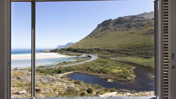 A view from a balcony overlooking a coastal landscape with a river, beach, and mountains.