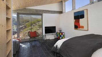 Ein modernes Schlafzimmer mit einem großen Bett, einem Fernseher und einem Fenster mit Jalousien.