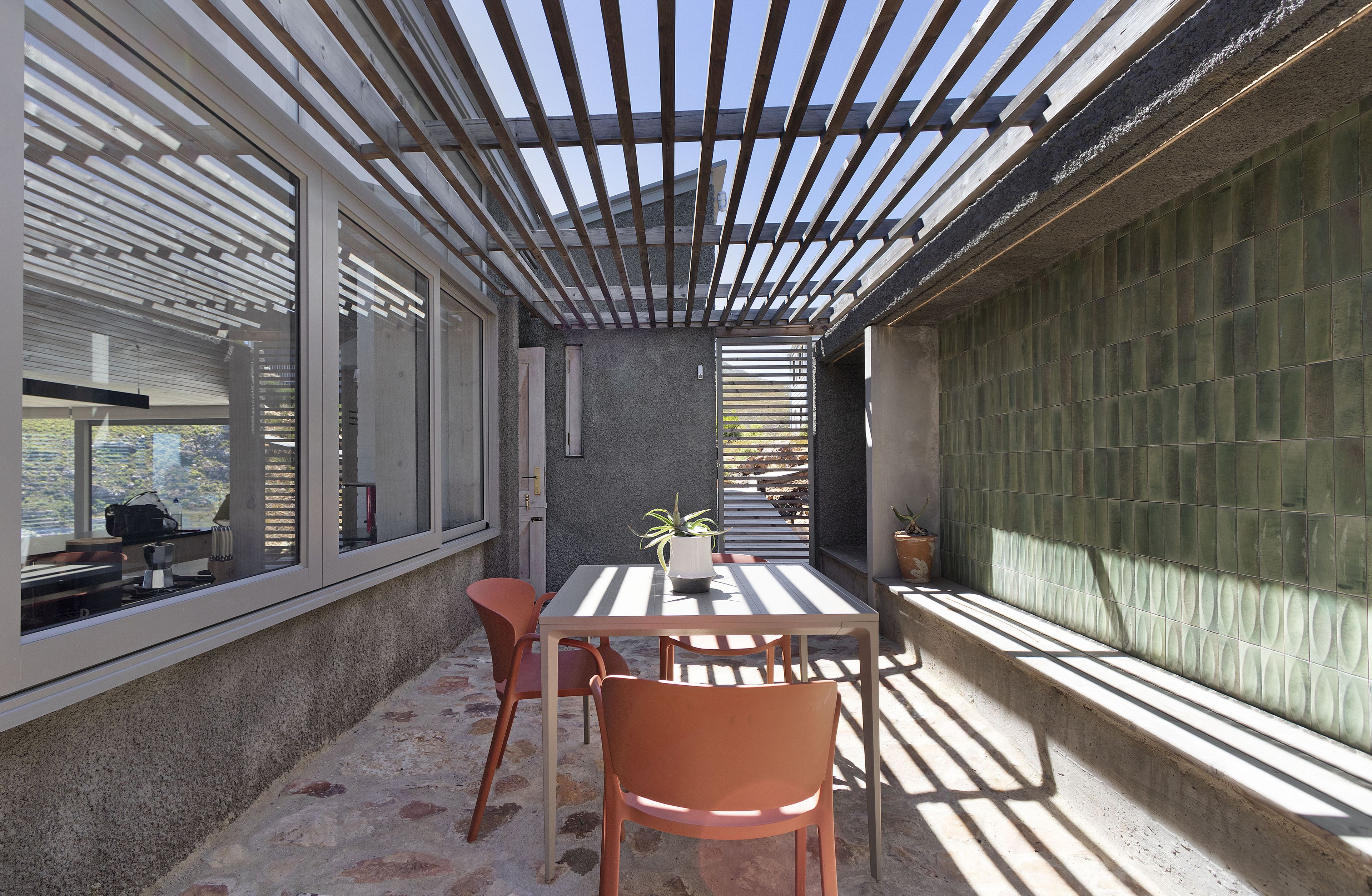 A covered patio area with a table and chairs, a potted plant, and a view through the windows.