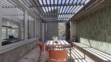 A covered patio area with a table and chairs, a potted plant, and a view through the windows.