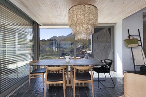 Un comedor moderno con una mesa grande y sillas, una lámpara colgante y vistas a montañas a través de amplios ventanales.