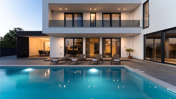 Una casa moderna de dos pisos con piscina, mobiliario exterior y ventanas amplias.