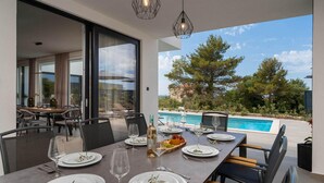 Un área de comedor al aire libre con vista a la piscina, muebles modernos y un cielo despejado.