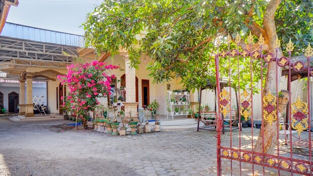 A courtyard with a paved area, a tree with pink flowers, and a metal gate. - OYO Life 92918 Rumah Kost Arrahma Syariah (Lengkong)