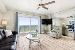 A living room with a glass table, a sofa, a chair, a TV, and a balcony with a view.