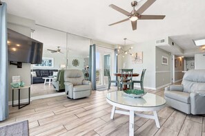Un vaste espace de vie doté d’un ventilateur de plafond, d’une table basse ronde en verre et d’un coin repas avec des chaises.