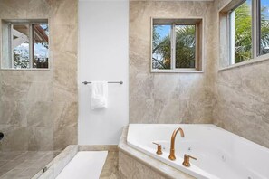 A modern bathroom with a large bathtub, a shower, and a window with a view of palm trees. - Welcome to The Betty!

 (Fort Lauderdale)