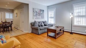 A living room with a grey sofa, wooden coffee table, and a dining area with a table and chairs. - NEW! Boston Condo Near MBTA, 3Mi to Fenway! (U1) (Boston)