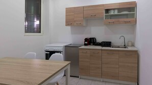 A compact kitchen with a stove, refrigerator, and wooden cabinets. - Phaedrus Living Heraklion City View Flat (Heraklion)