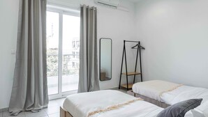 A hotel room with two beds, a large window with curtains, an air conditioning unit, and a mirror on the wall. - Phaedrus Living Heraklion City View Flat (Heraklion)