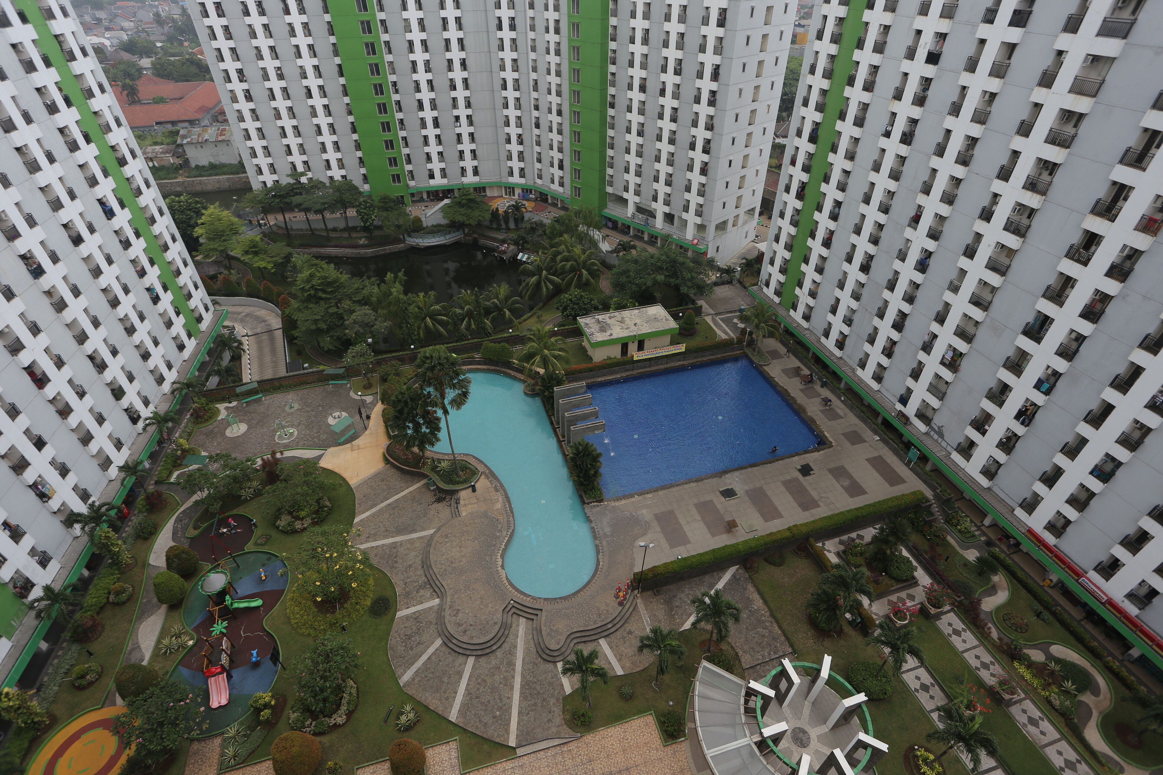 A high-rise residential building with a swimming pool, playground, and landscaped garden areas.