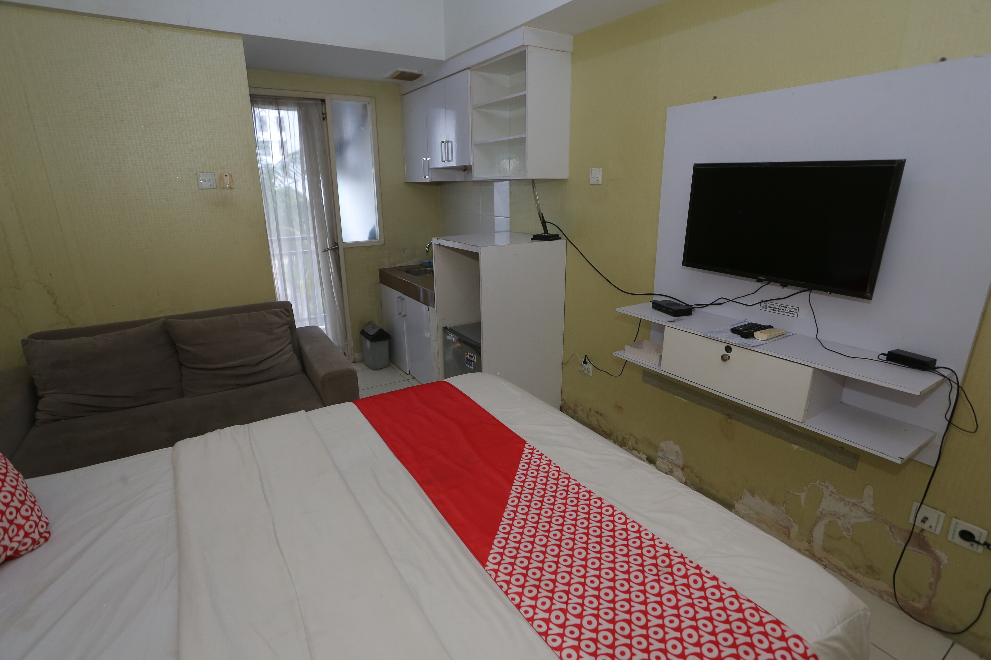 A hotel room with a bed, a TV mounted on the wall, a desk, and a wardrobe.