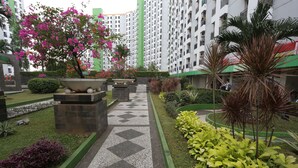 A courtyard with a patterned walkway, potted plants, and a tall building in the background. - OYO Life 93008 Pelangi Coliving (Tangerang)
