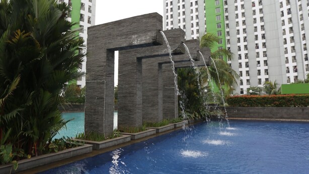 A swimming pool with a waterfall feature, surrounded by tall residential buildings. - OYO Life 93008 Pelangi Coliving (Tangerang)