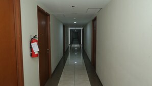 A long, narrow hallway with wooden doors on either side, a fire extinguisher mounted on the left wall, and a tiled floor. - OYO Life 93008 Pelangi Coliving (Tangerang)