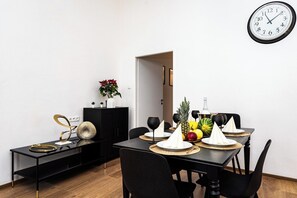 Un coin repas avec une table noire dressée pour quatre personnes, un canapé noir, un meuble noir pour la télévision et une horloge murale.