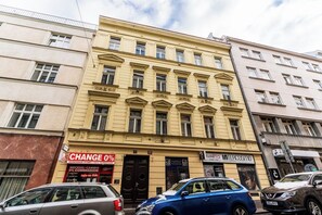 Un immeuble à plusieurs étages, doté d’une façade jaune bien visible, d’une porte d’entrée noire et d’une enseigne indiquant un service de change de devises.