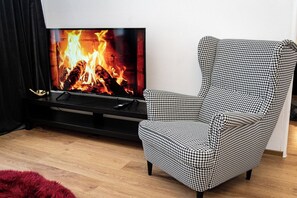 A living room with a television displaying a fireplace, a houndstooth patterned armchair, and a red furry rug.