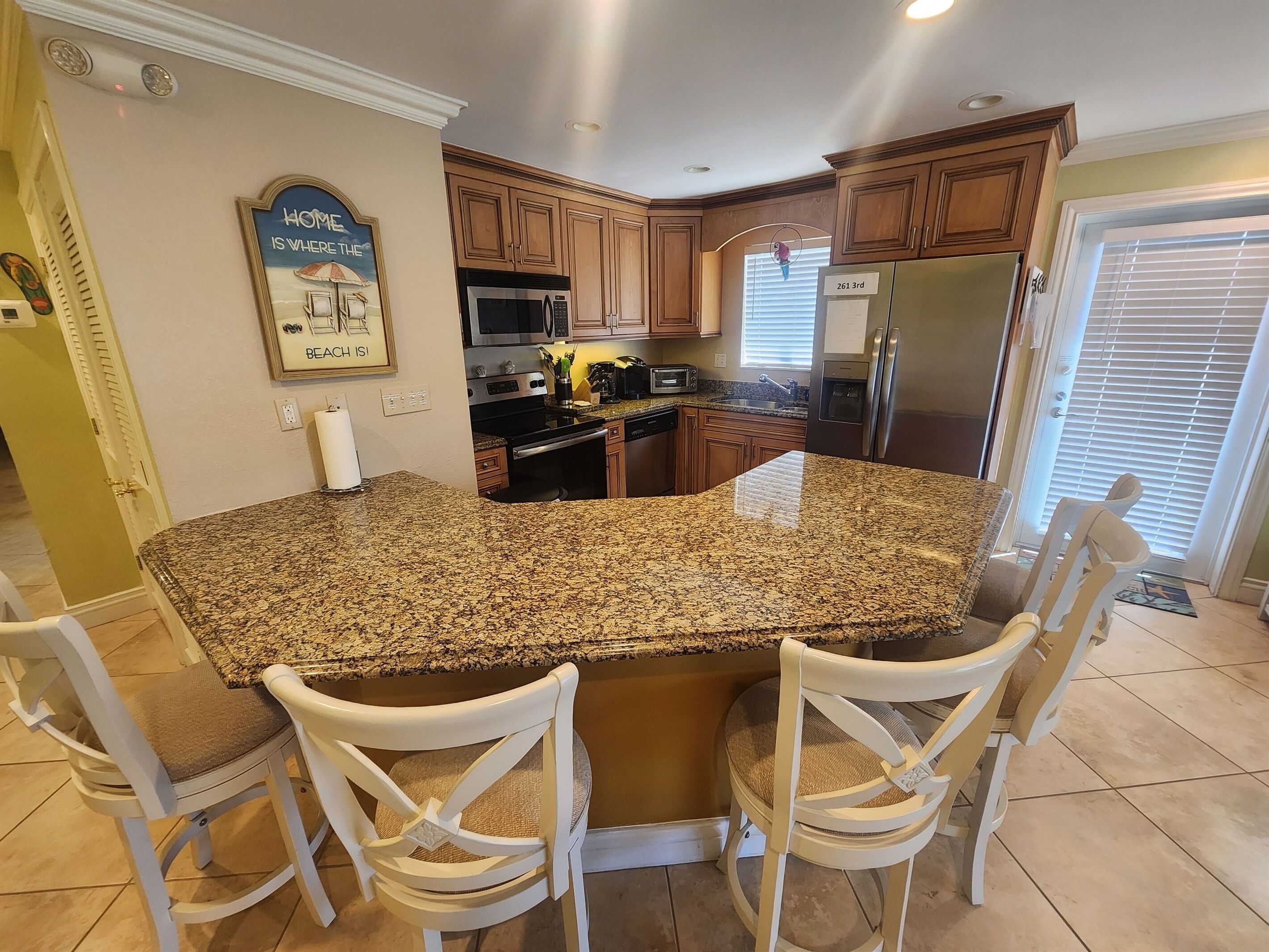 A kitchen with granite countertops, wooden cabinets, a stainless steel refrigerator, and a built-in microwave.