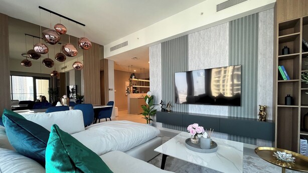 A modern living room with a large flat-screen TV, a sofa set, a dining area, and a kitchen in the background. - Luxury Burj Royale 4bed With Balcony Burj Khalifa Fountain View (Dubai)