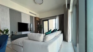 A modern living room with a white sofa, a flat-screen TV, and a large window with curtains. - Luxury Burj Royale 4bed With Balcony Burj Khalifa Fountain View (Dubai)