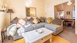 A living room with a grey sofa, a white coffee table, and a dining area with a wooden table and chairs.