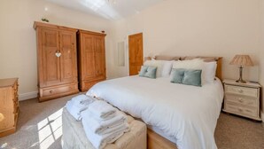 A bedroom with a large bed, wooden wardrobe, and a nightstand with a lamp.