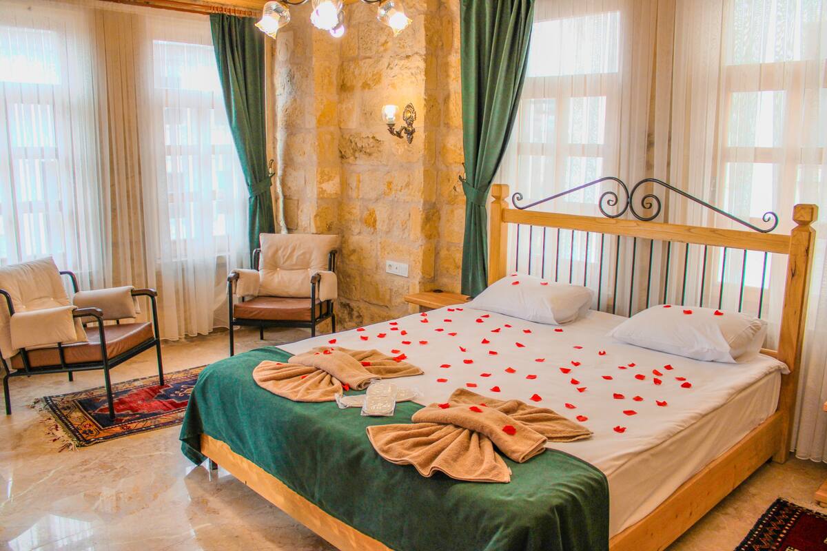 A hotel room with a large bed, two chairs, a wooden headboard, and a stone wall.