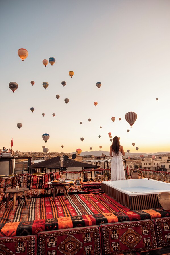 A rooftop terrace with a woman in a white dress overlooking a cityscape with numerous hot air balloons. - Tantan Cappadocia House (Nevsehir)